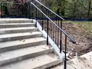 Black metal handrail alongside outdoor concrete steps.