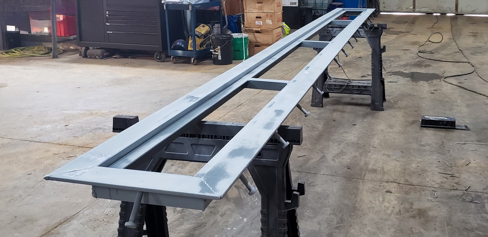 Long custom steel frame supported on fabrication stands in the shop.