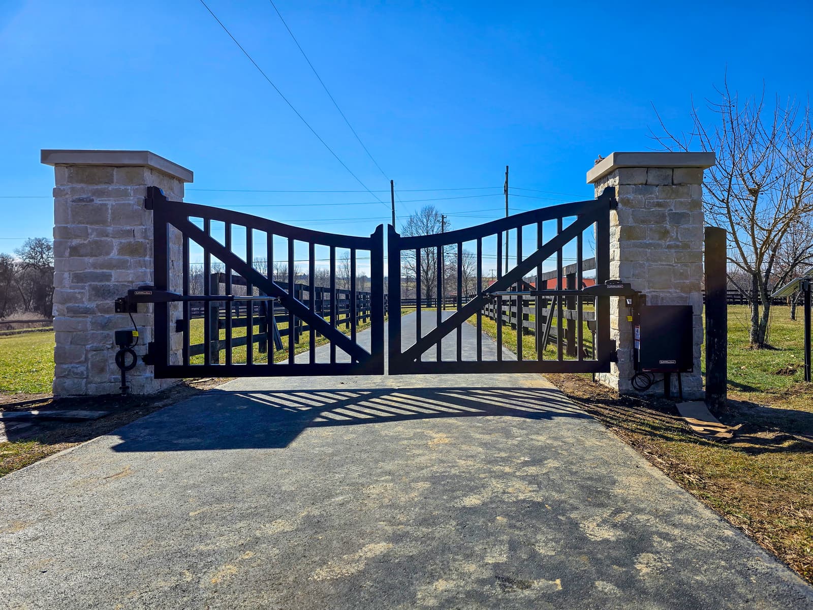 Finished custom metal driveway gate with stone columns and automated opener hardware in Central Kentucky.