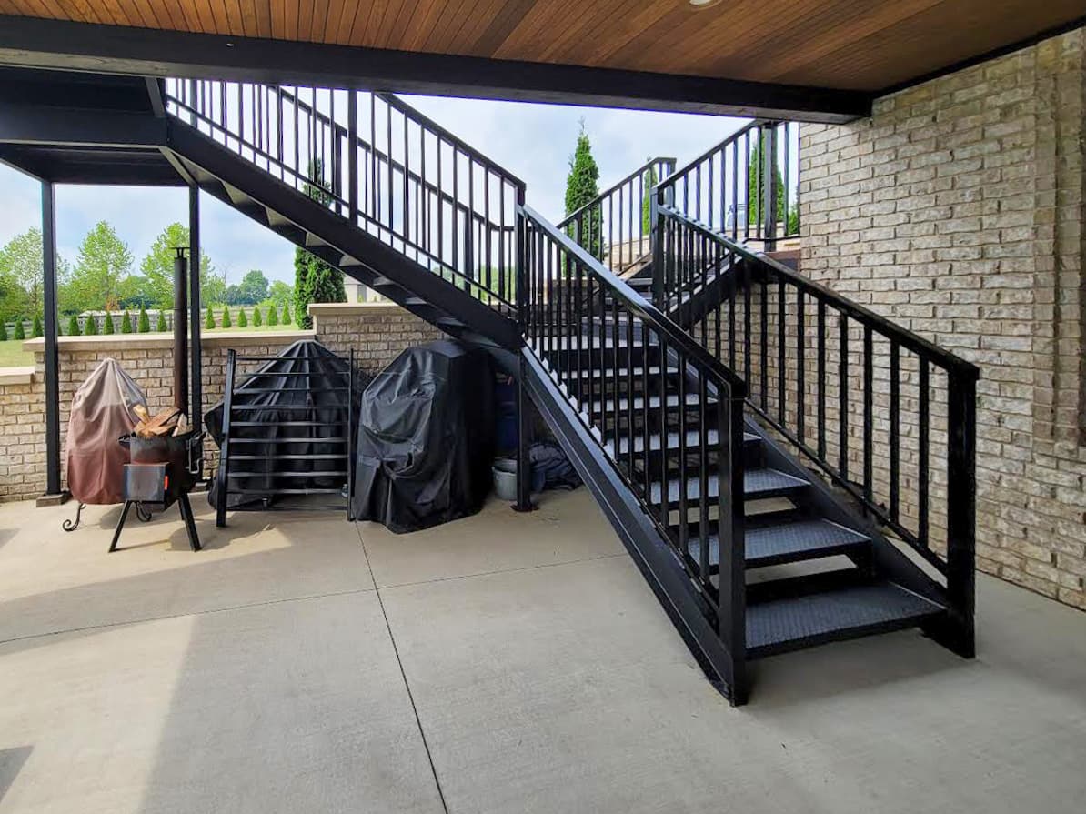Black exterior metal stairs and handrails connecting a covered deck to the yard.